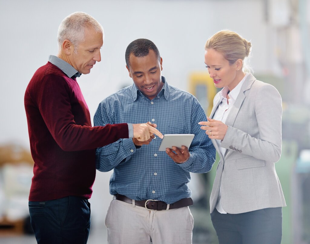 A collaborative team of business leaders and operations managers review digital data and performance metrics on a tablet together during a workplace consultation.