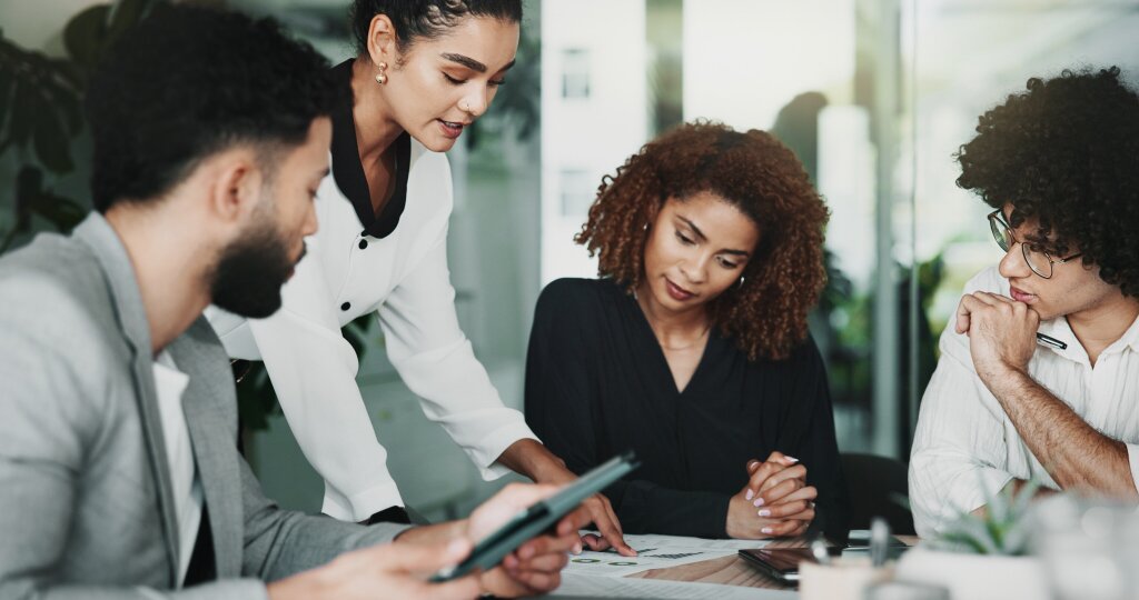 An effective business leader directs a collaborative team meeting, guiding her diverse group of executives through strategic planning documents in a corporate boardroom.