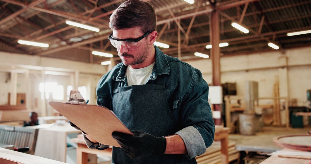 An operations manager reviews a safety and inventory checklist on a clipboard to ensure smooth manufacturing workflow and quality control on the workshop floor.