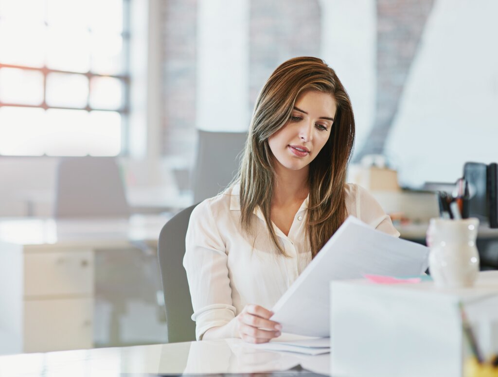 A business administration trainee looks up thoughtfully while working on a project assessment on her laptop.