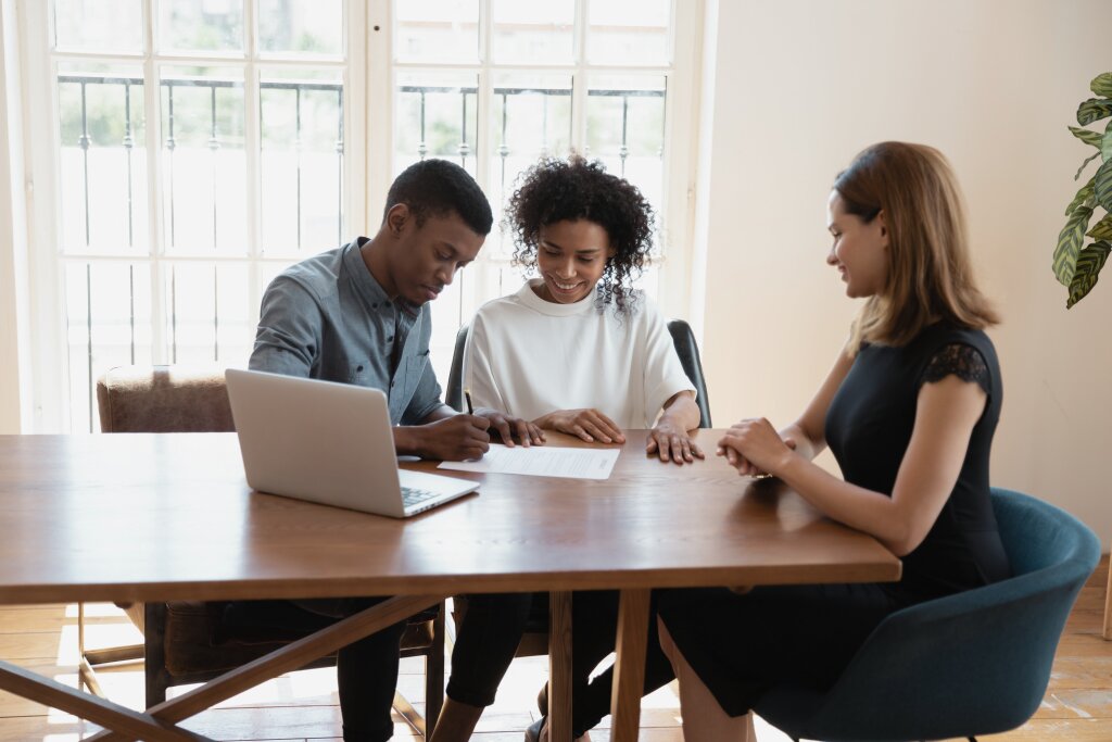 A financial services specialist assists a young couple during a consultation as they finalize and sign their financial planning or loan documents.