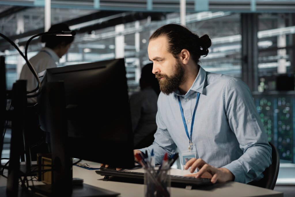 A focused network administrator or IT specialist monitors network traffic and configures system security protocols at a desktop workstation in a operations center.