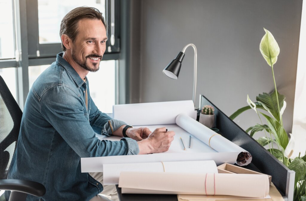 A professional project manager or project coordinator reviews architectural drawings and project schematics to plan timelines and manage construction deliverables at his desk.