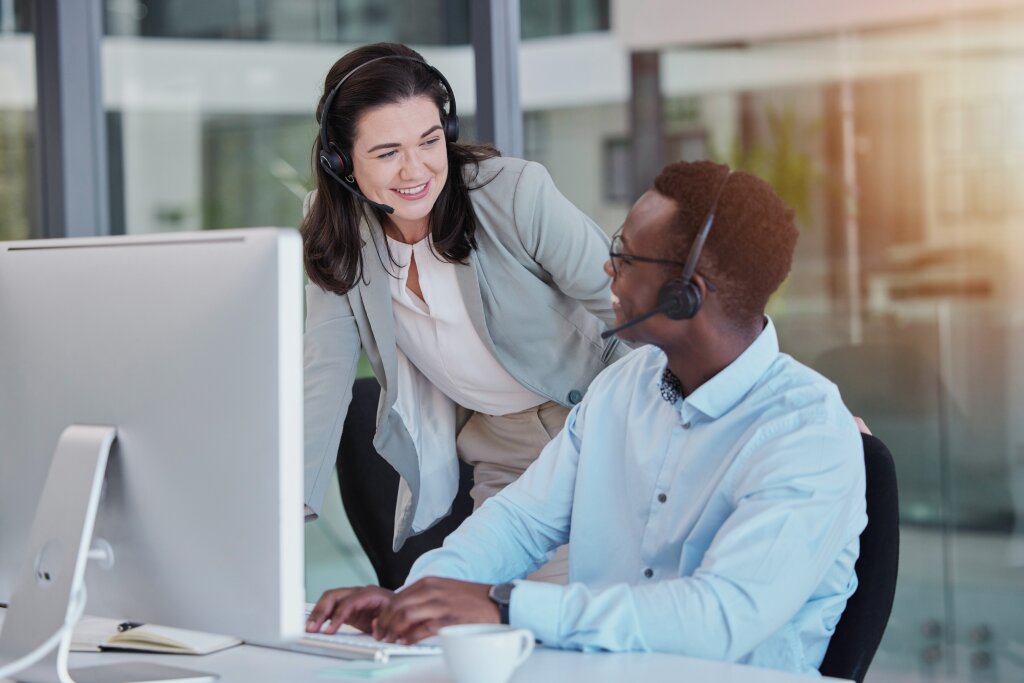 A training mentor supports an online business student at his computer workspace during a collaborative helpline coaching session.
