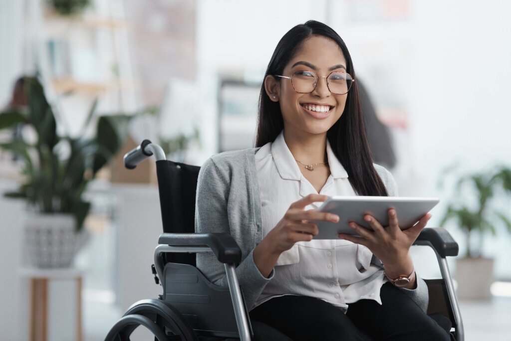 A smiling adult student using a wheelchair holds a digital tablet while engaging in self-paced learning or an online training course.