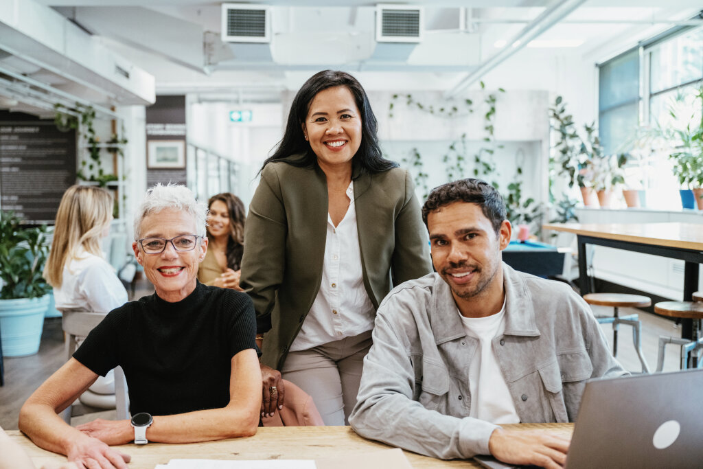 A multi-generational team of trainees and a supervisor smile at a desk, showcasing diversity in corporate workforce training.