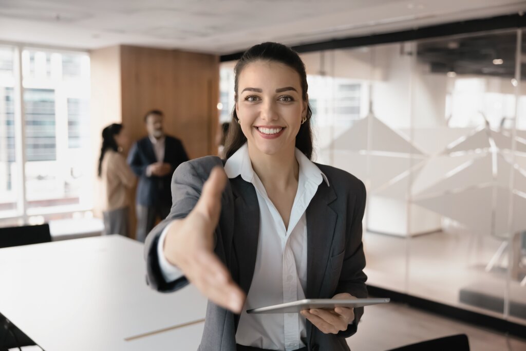 A smiling employer extends her hand to welcome a successful graduate to her organization after a placement interview.