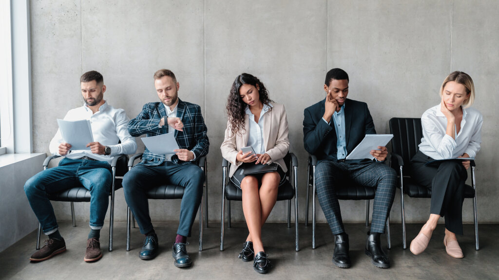 A group of graduates wait in a reception area, reviewing their documents before starting their formal employment placement interviews.