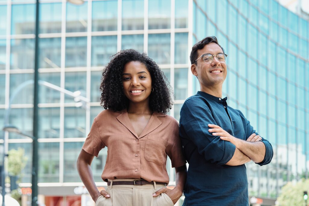 Two smiling young trainees stand confidently outside a city campus, eager to begin their vocational traineeship program.