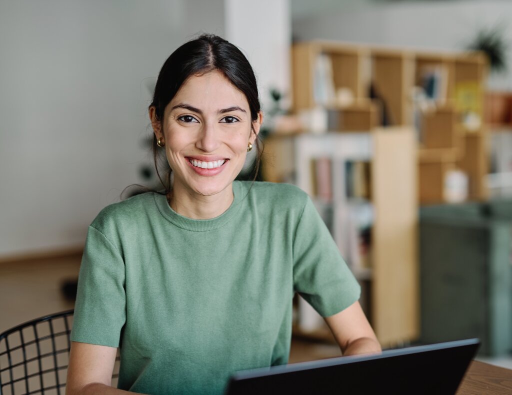 A smiling adult student sits at a workspace with an open laptop, engaging in flexible study or online vocational training.