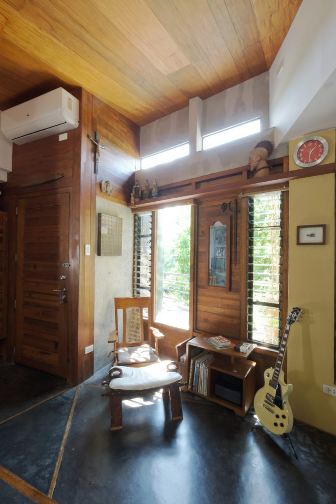 A living area with clerestory windows, a wooden lounge chair, and a guitar.