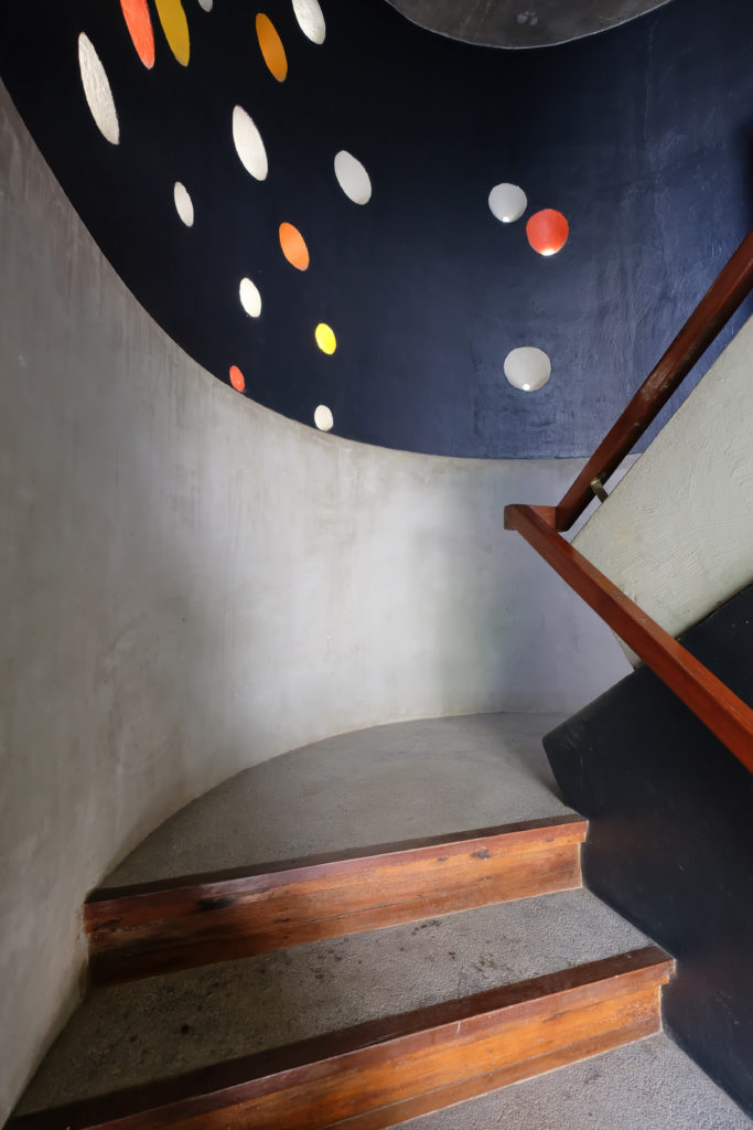 A concrete stairwell with wooden banister and curved blue ceiling.