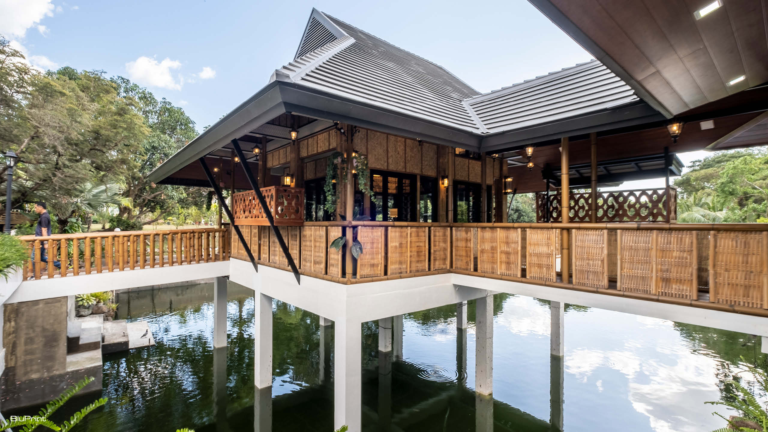 A modern bahay kubo with concrete stilts and pitched roof built above a lake.