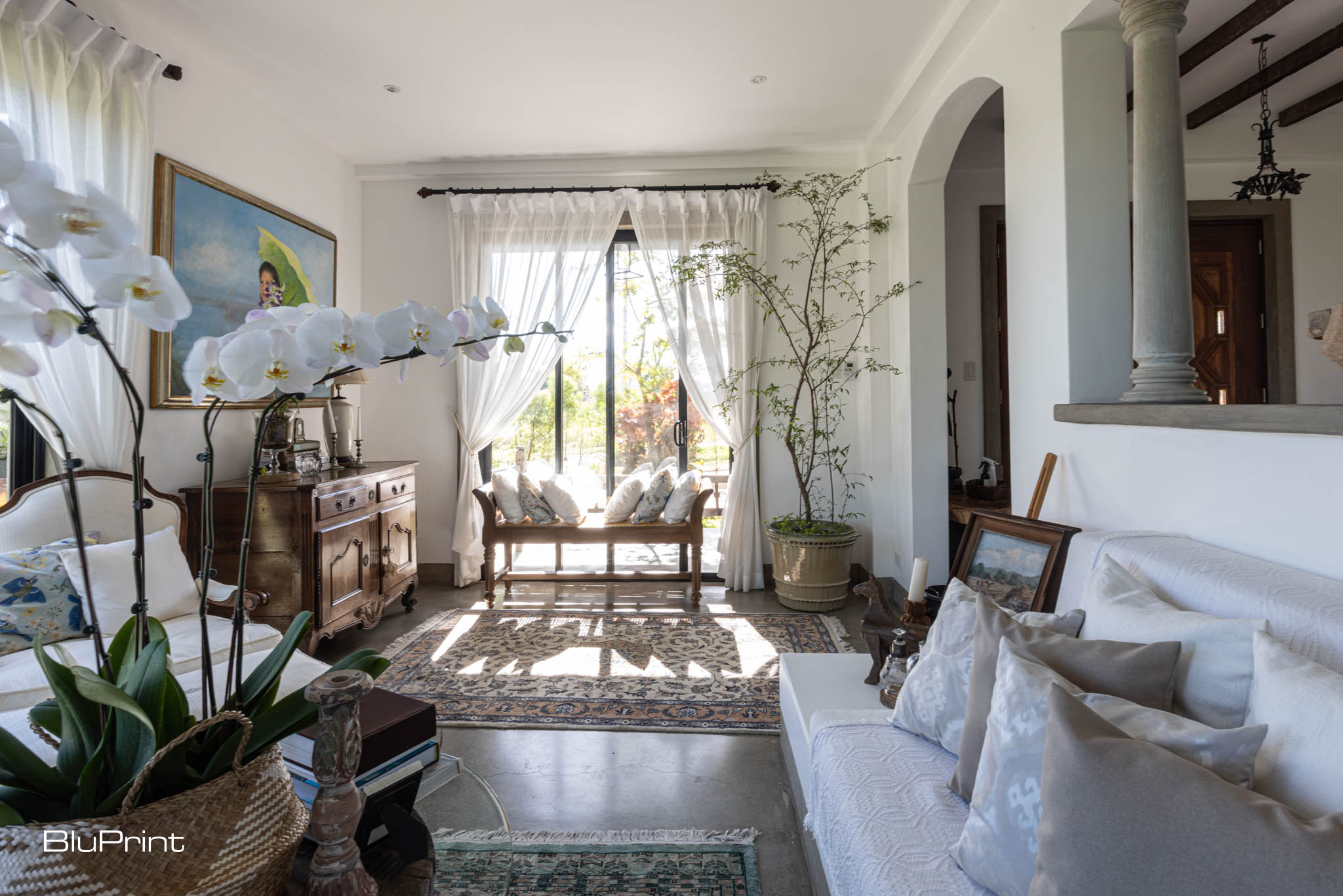 View of a modern home living room with a large white sofa, patterned rugs, and traditional wooden furniture pieces.