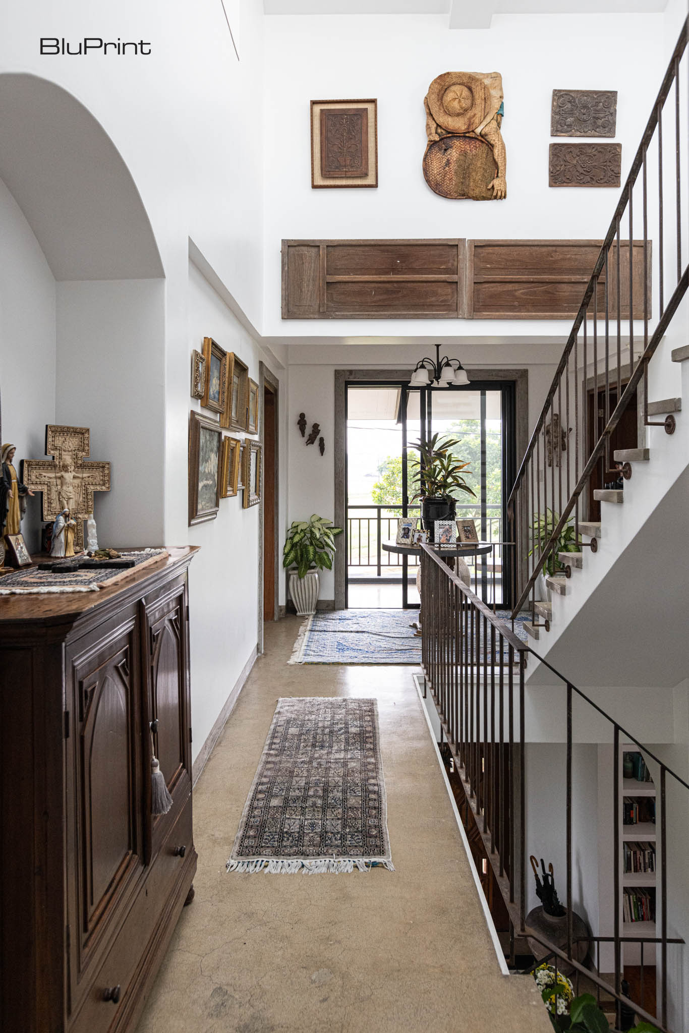 View of a second floor with the stairwell on the side. A large antique cabinet sits along the hall, which has a long carpet runner. A large sliding door looks out into the outdoor area.