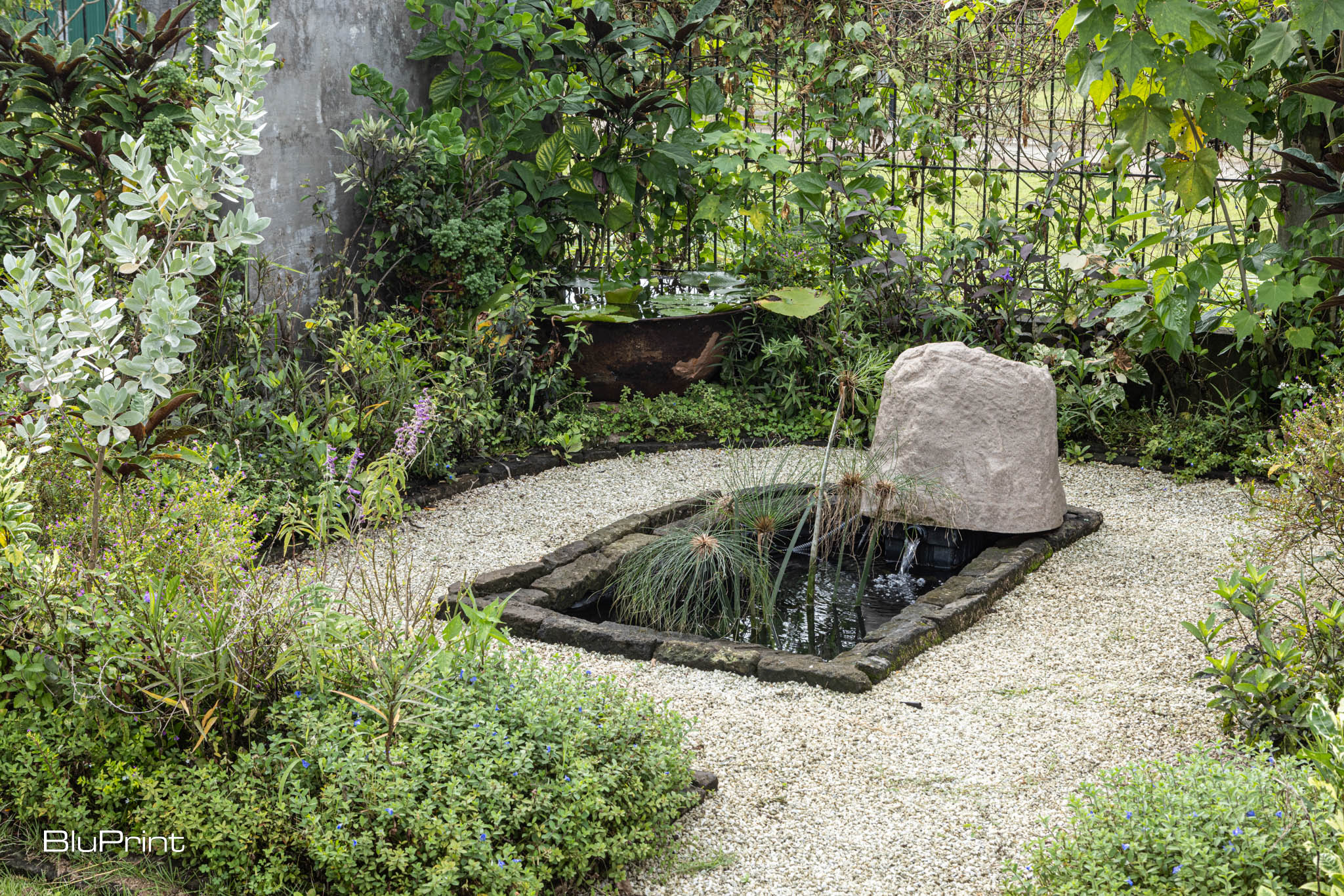 AA large white rock sits on the edge of a small pond surrounded by pebbles and greenery.