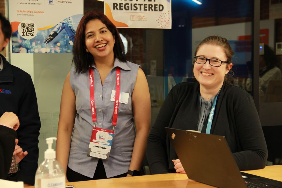 Two woman smiling at camera, both wearing GovHack lanyards