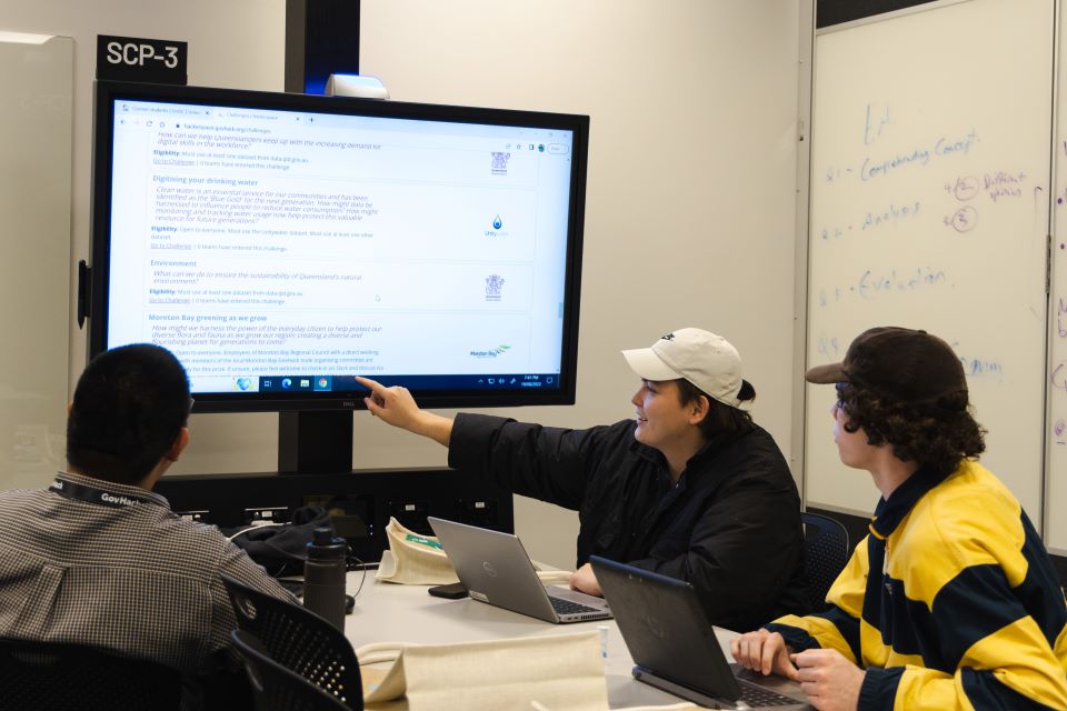 Three people at a table around a big screen