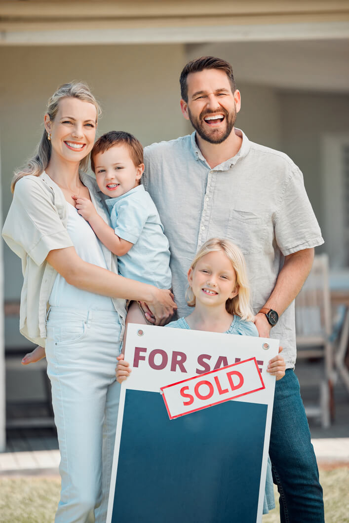 Happy family standing outside their new home with a sold sign