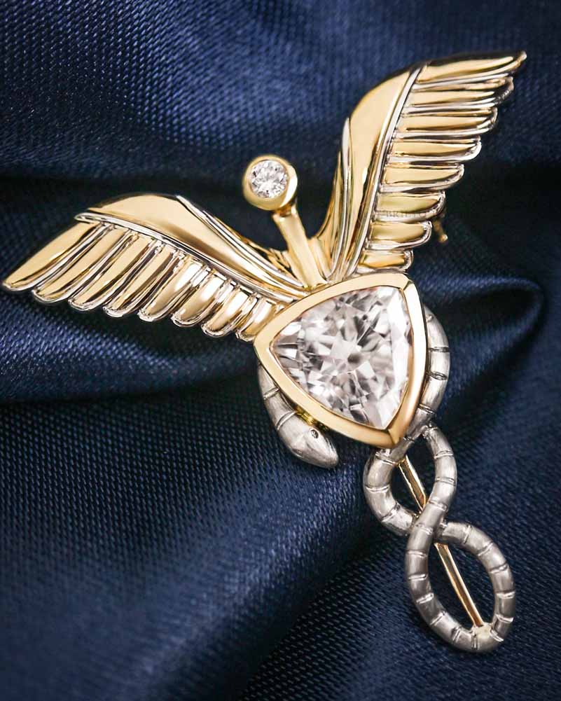 The Caduceus Brooch in white and yellow gold with round diamond accents