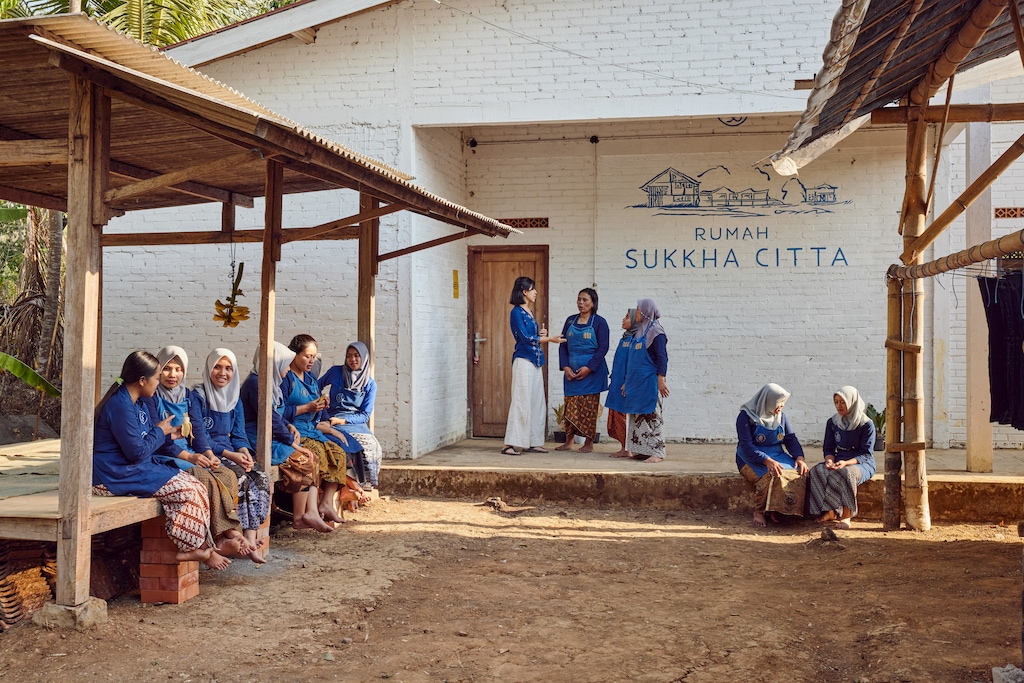 Denica Riadini-Flesch (wearing white pants), the recipient of the 2023 Rolex Award for Enterprise, speaks with women at a SukkhaCitta craft school. ©Rolex / Sébastien Agnetti
