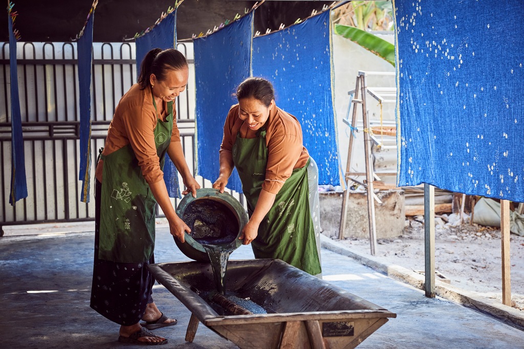 Ibu Sri and Ibu Muntiani prepare a bath for dyeing fabrics in one of SukkhaCitta's craft schools in Rumah, East Java. The textiles hanging behind them are decorated with floral batik designs. 
©Rolex / Sébastien Agnetti
