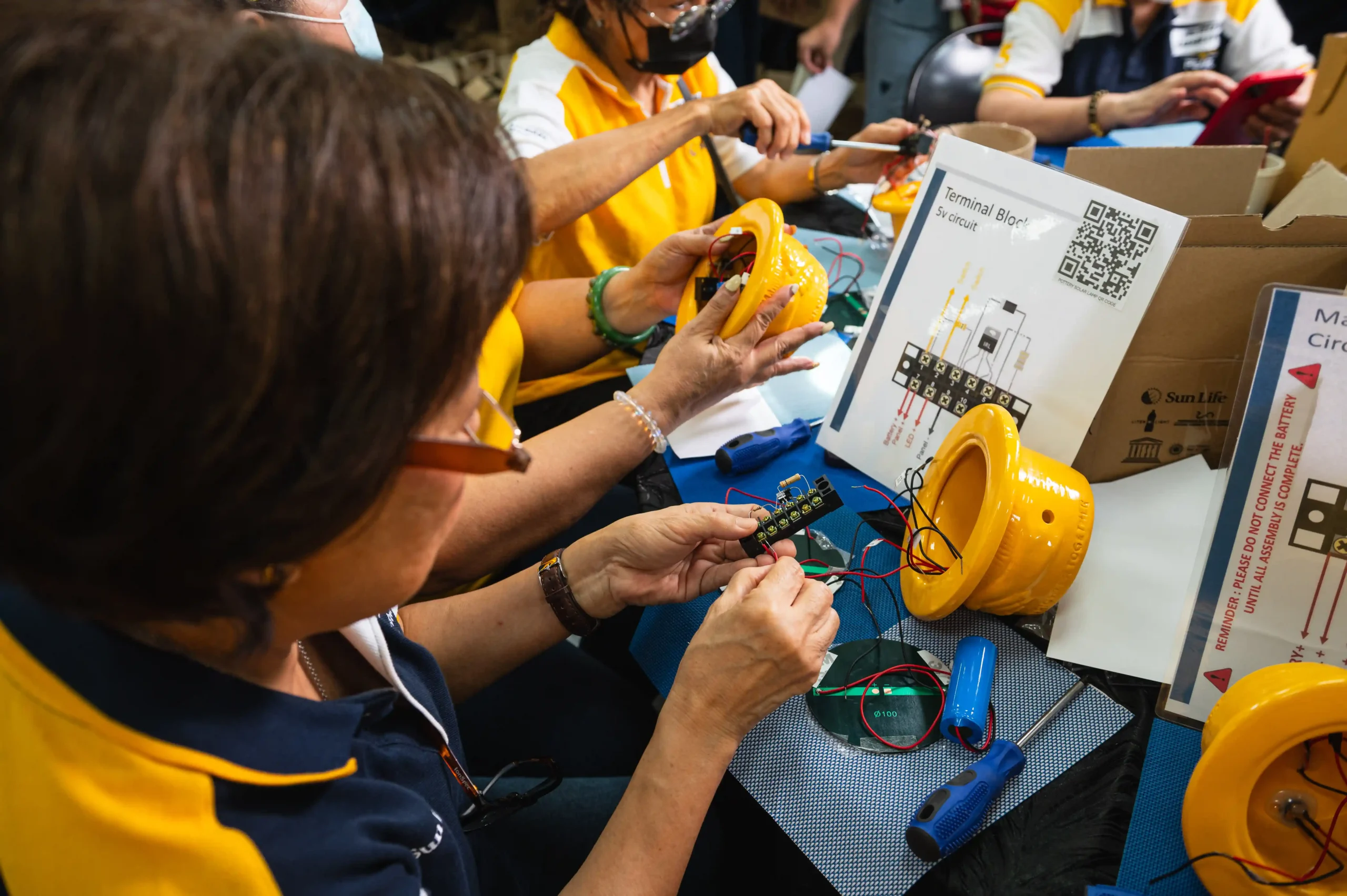 Community volunteers follow a step-by-step guide to assemble solar lamps/Photo by Derrick Lim