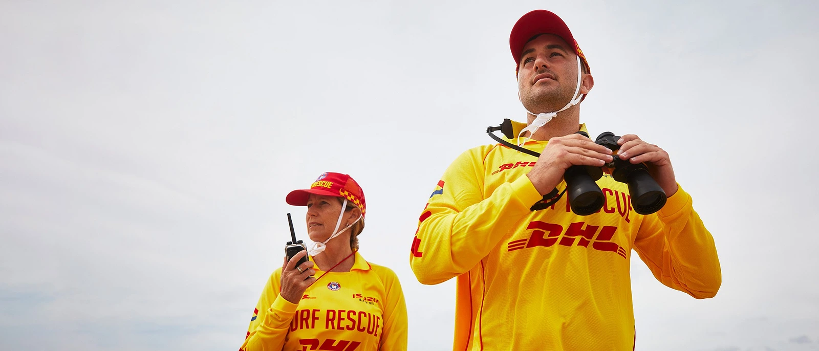Two surf lifesavers on patrol, one using a radio and one with binoculars