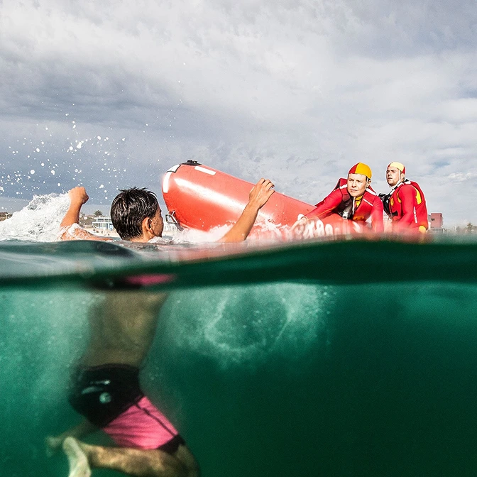 Split-level view of a surf lifesaver swimming out with a rescue tube