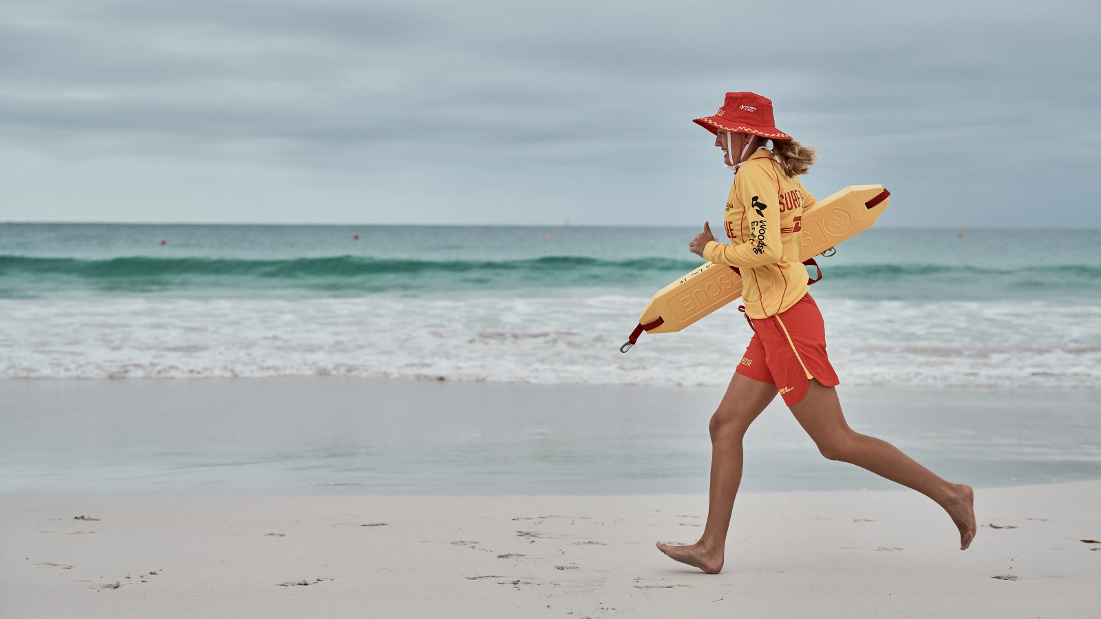 A surf lifesaver running along the beach with a rescue board