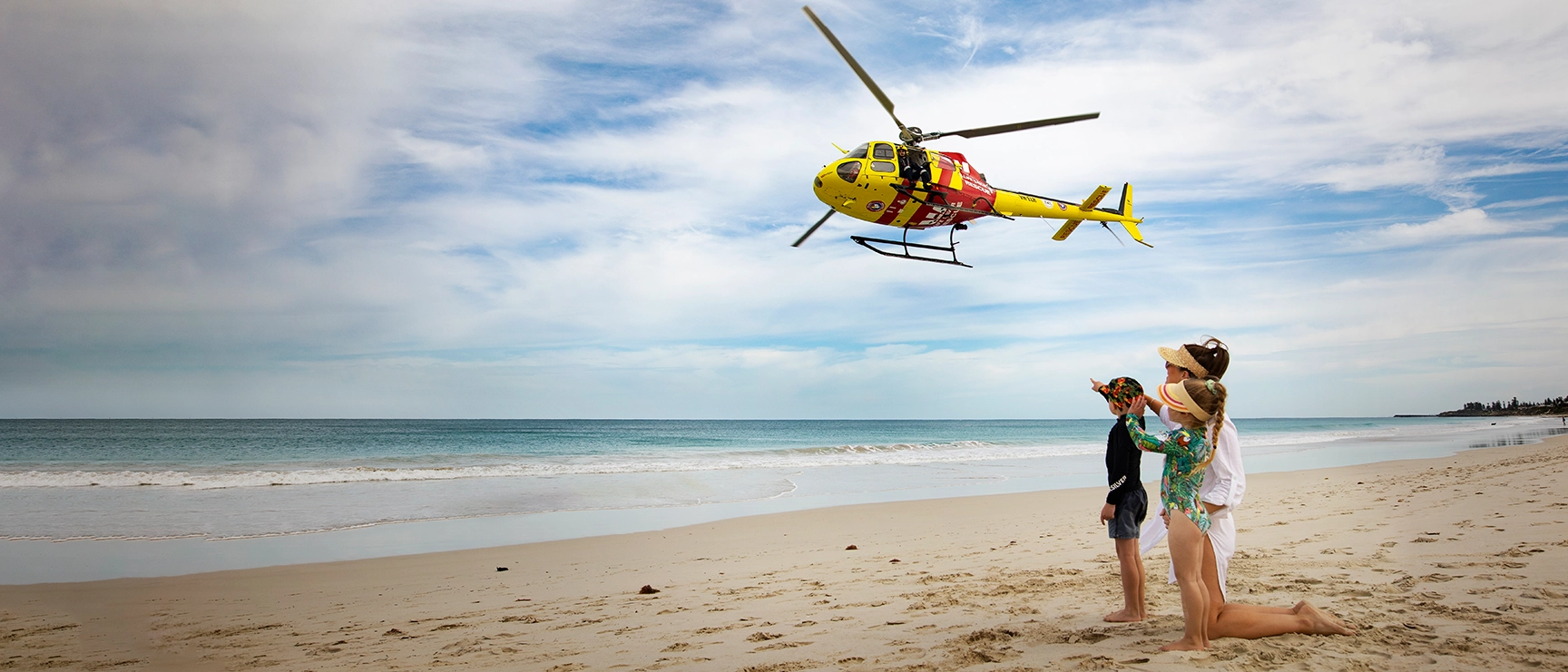 A family on the beach watching the Westpac Life Saver Rescue Helicopter fly overhead