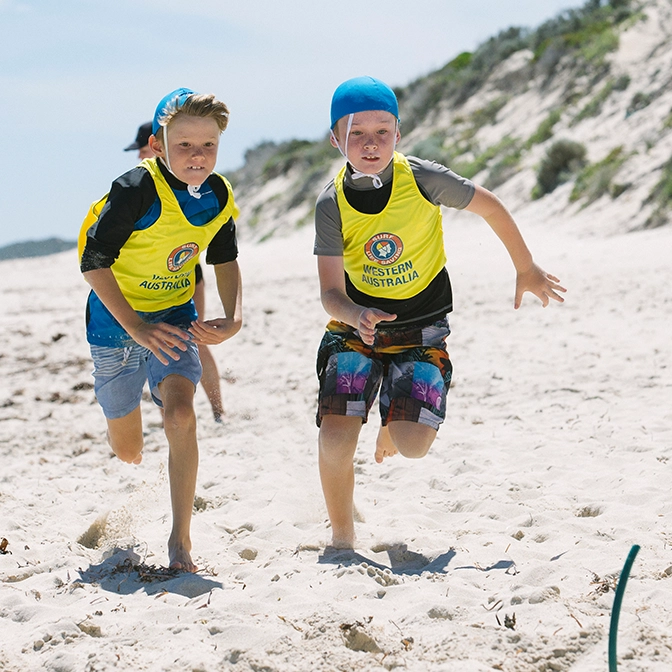 Two children in Nippers vests running along the beach