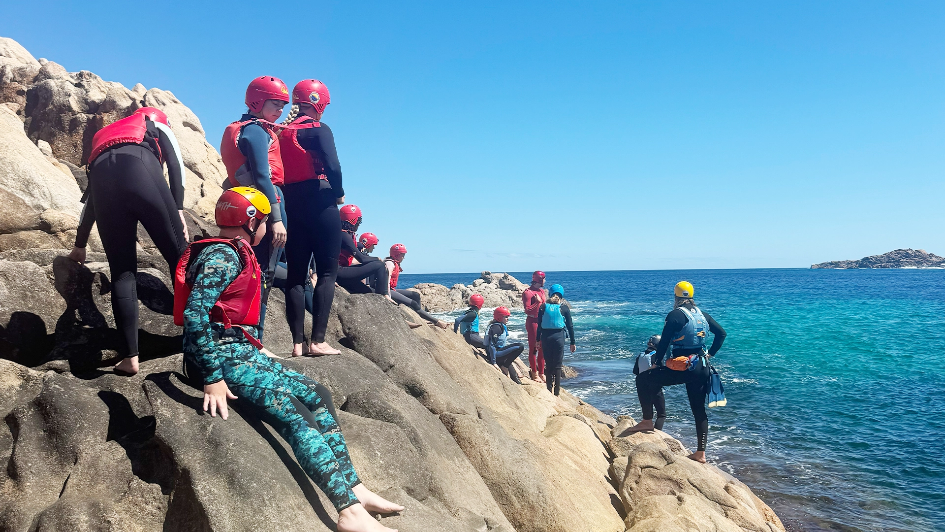 Youth camp participants climbing on coastal rocks
