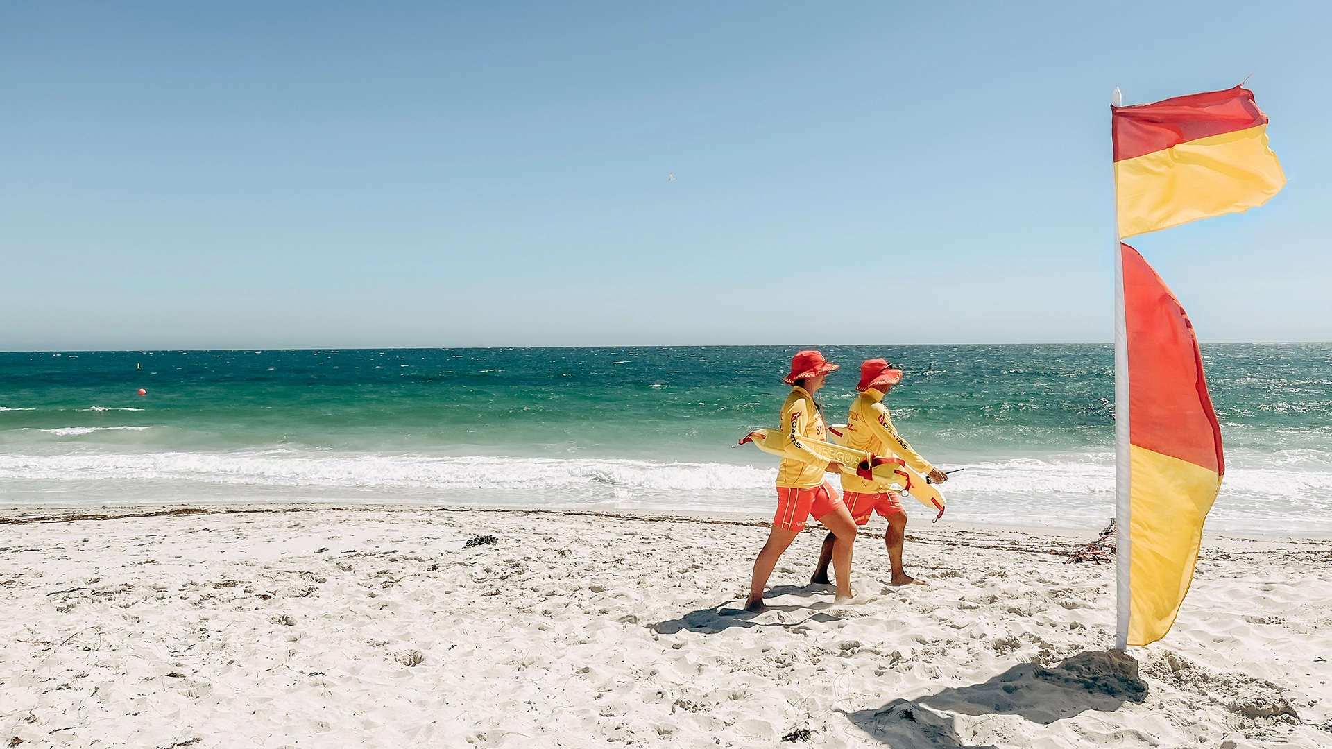 Two surf lifesavers walking the beach beside the patrol flag