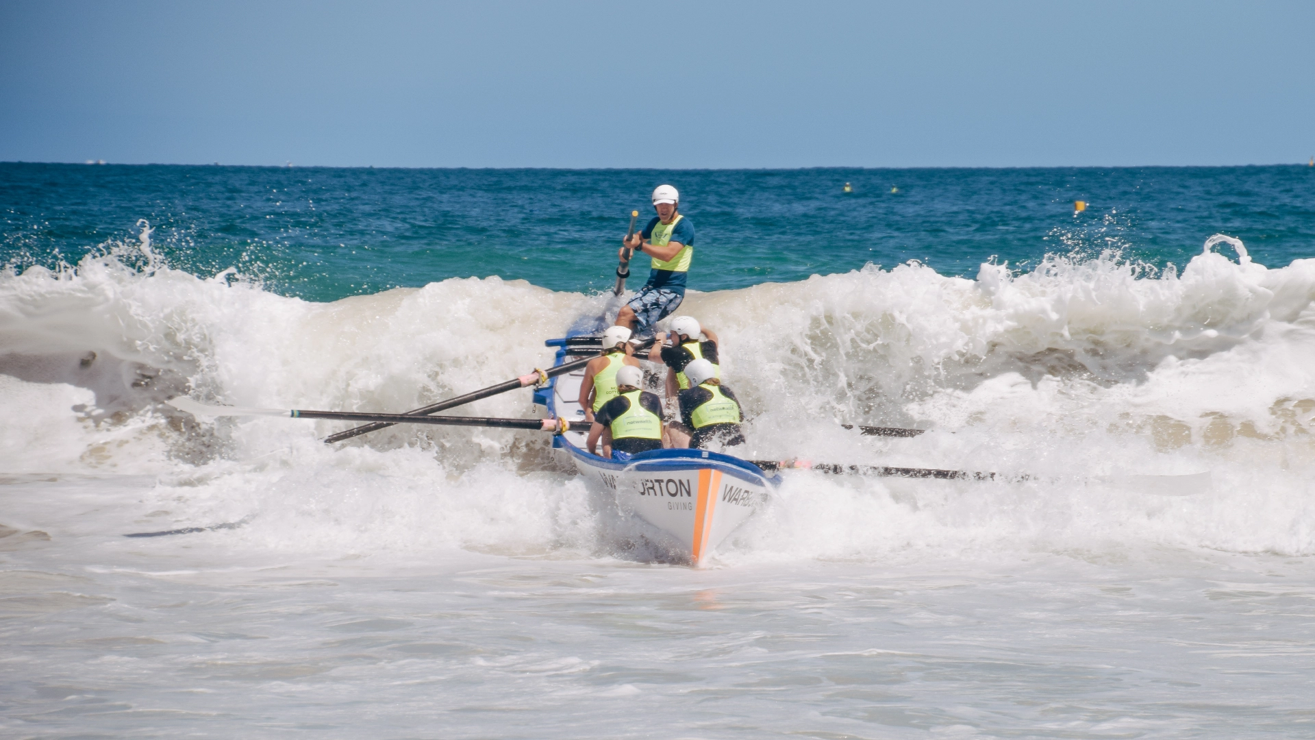 A surfboat crew rowing out through the surf