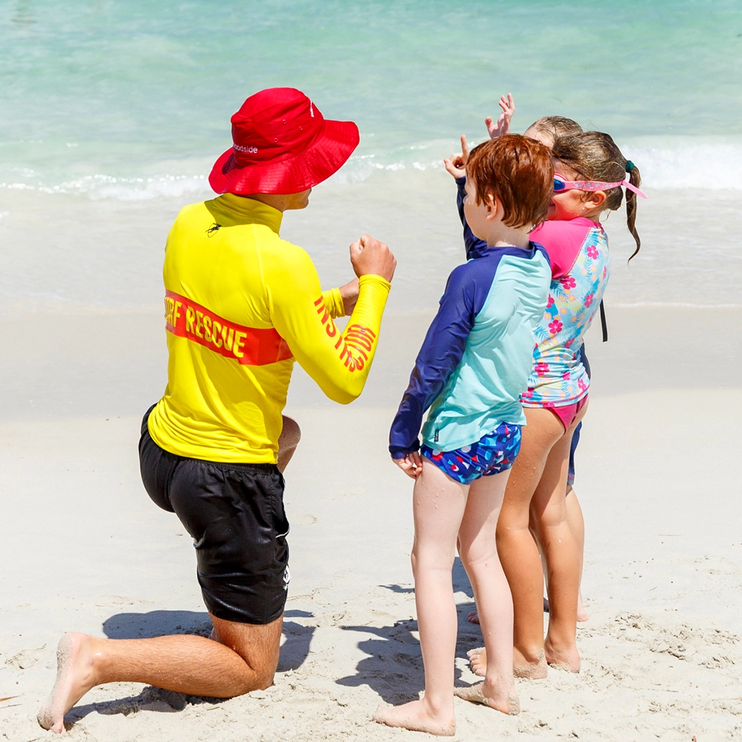 A surf lifesaver talking with two children on the beach
