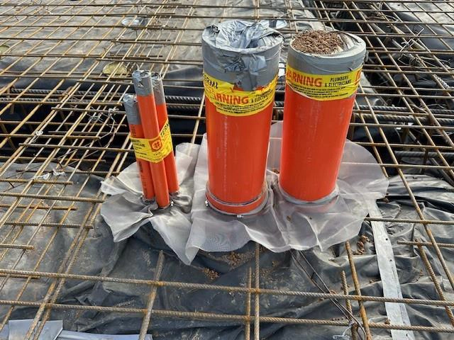 A Termiflange collar installed around a cluster of orange pipes which will penetrate through the concrete substrate.