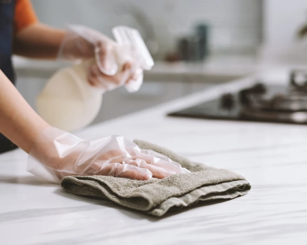 A woman with a spray bottle wiping down a kitchen counter