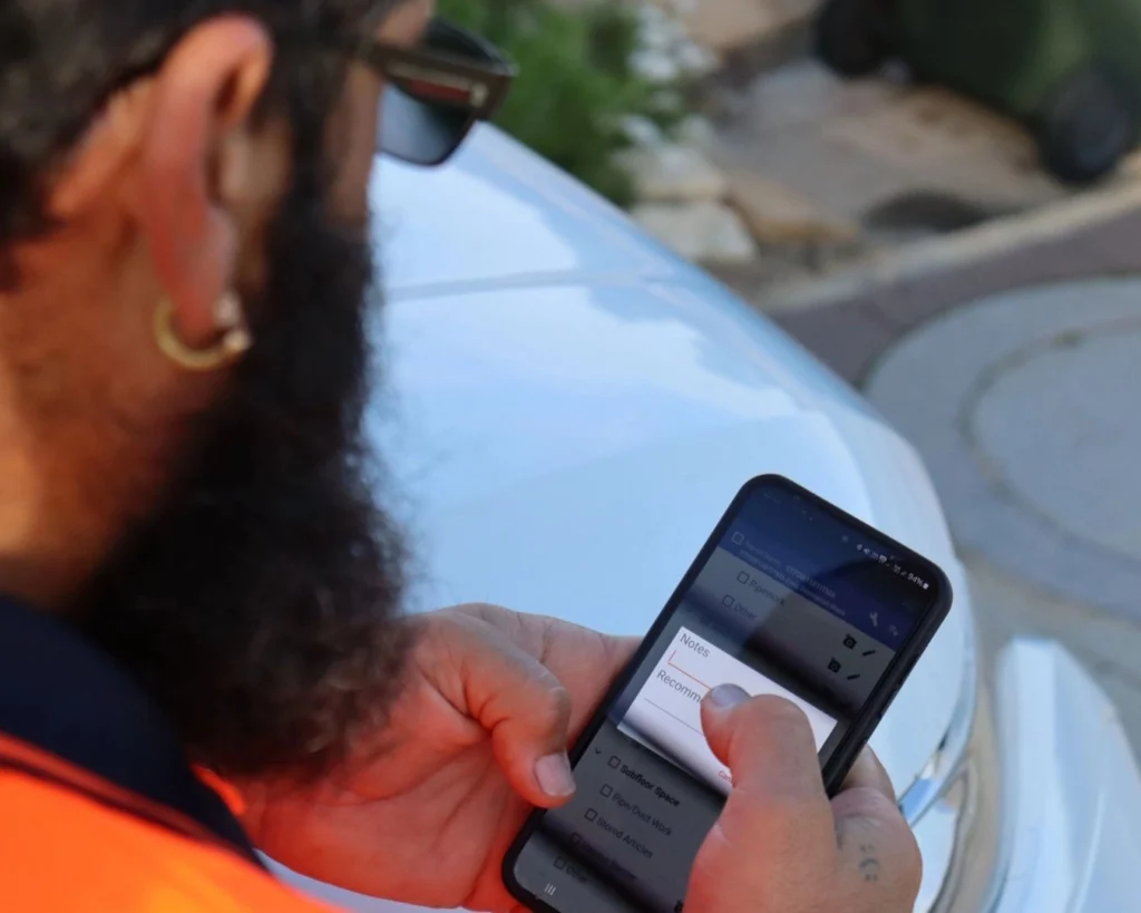 Termitrust Pest Control technician completing a timber pest inspection report on a mobile phone