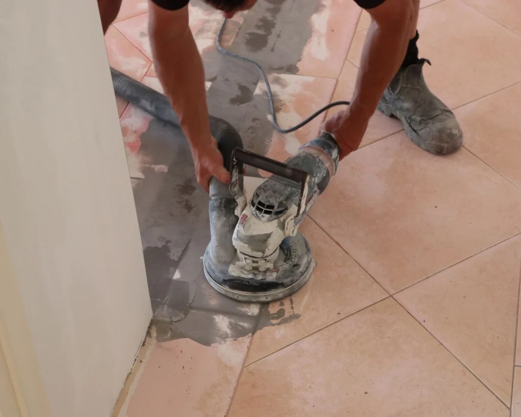 Epoxy flooring applicator using a handheld grinder to level out patch work previously completed on the tile floor