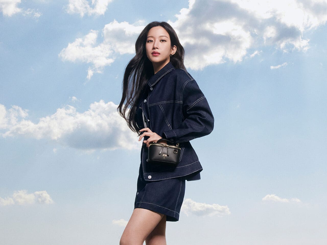 Mun Ka-Young wearing a denim jacket and denim shorts with knee-high boots and Lex Small Train Case crossbody from the TUMI Voyageur collection.