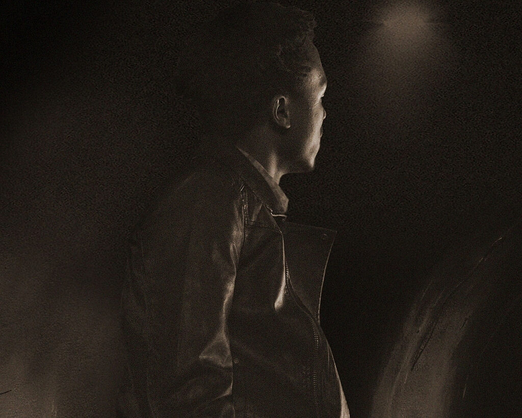An shadowy image of the back of a man against a dark background.