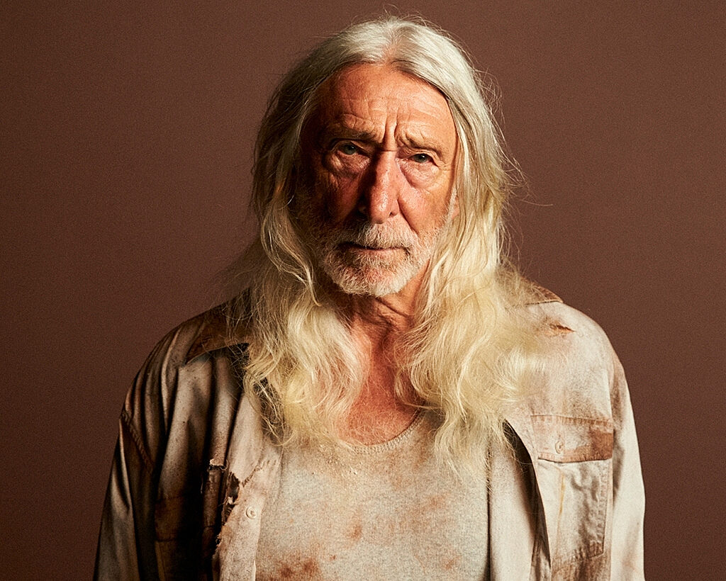 Close up of a stern old man with long white hair, wearing stained clothing.