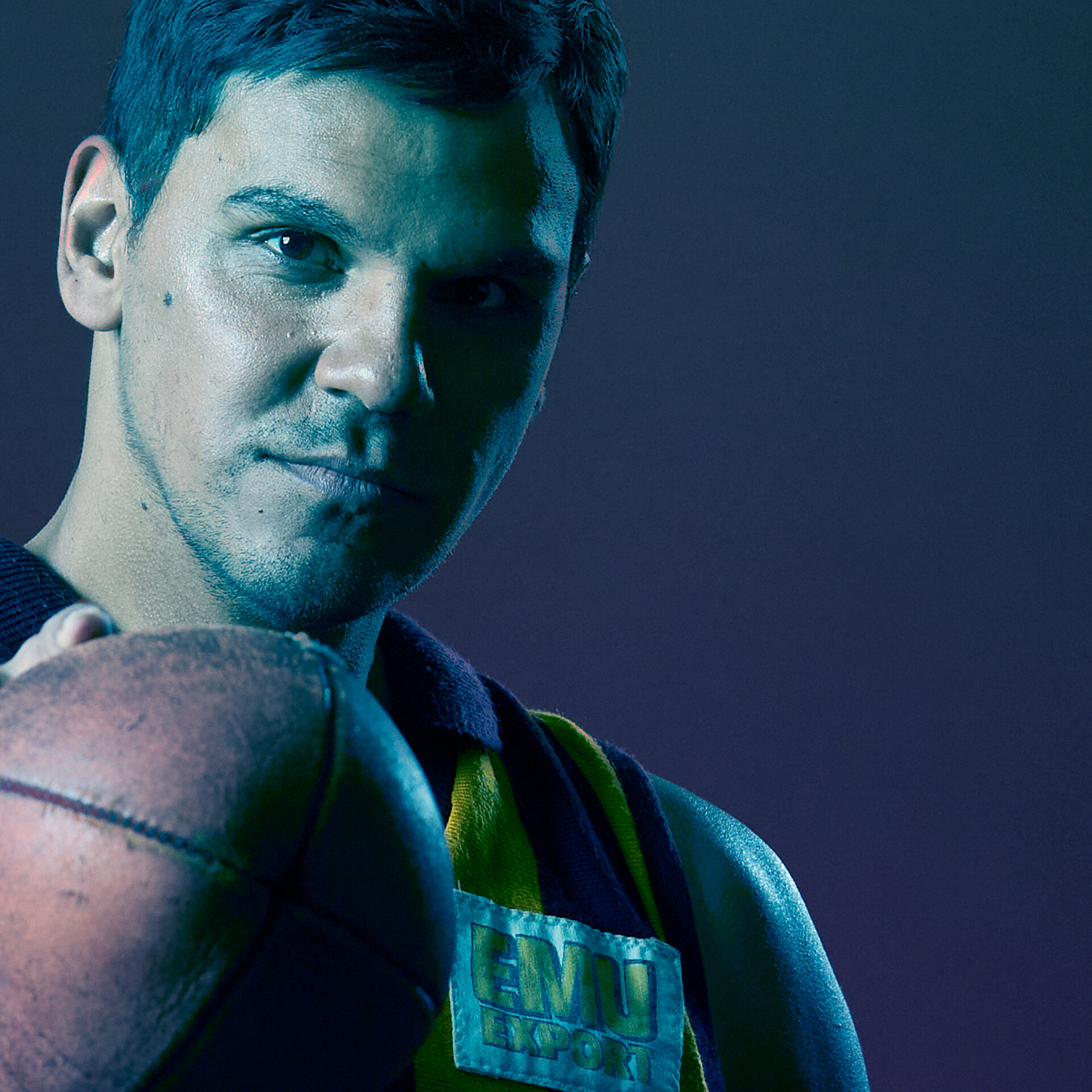 A man holding an AFL football, staring straight to camera.