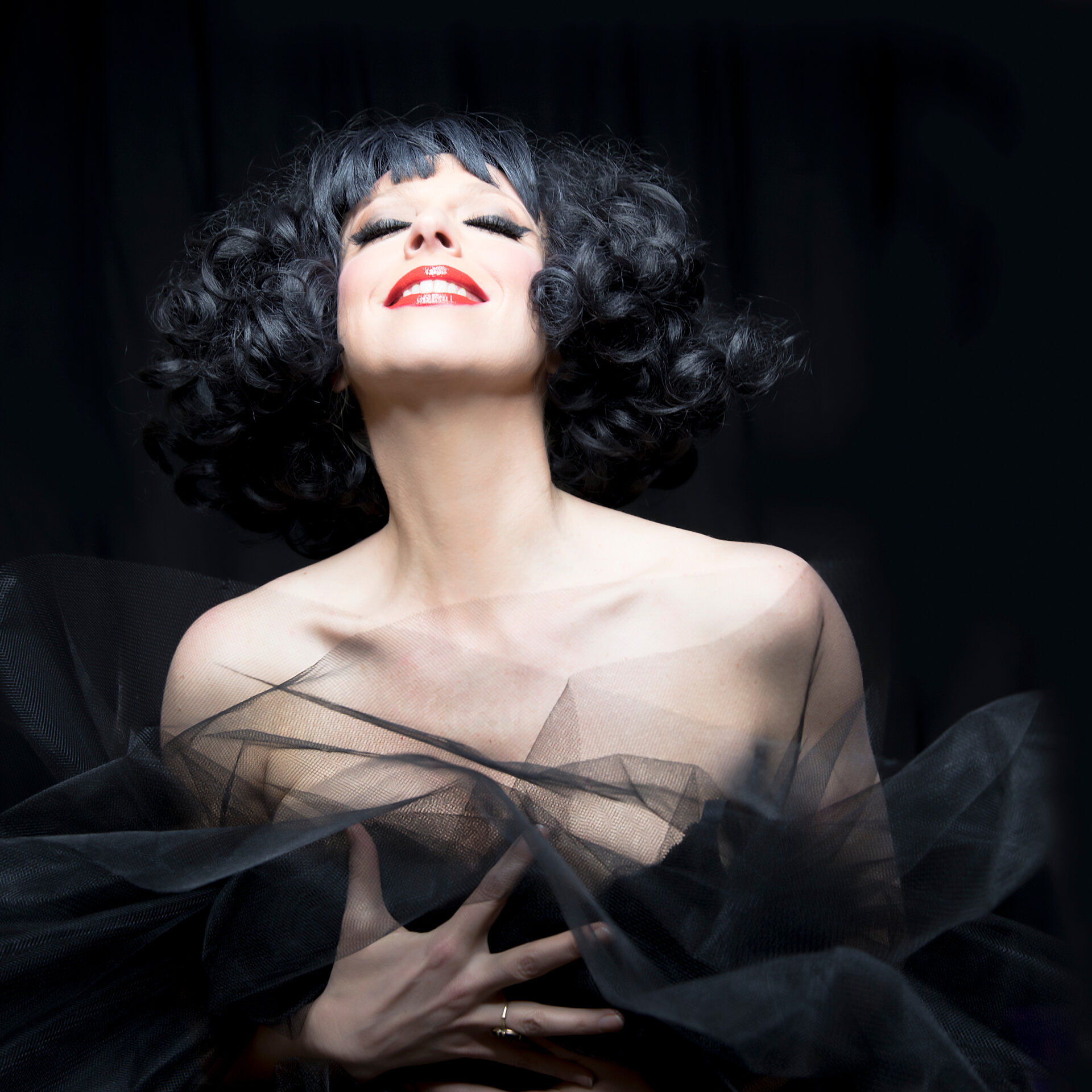 Close up of a woman with curly black hair wearing a black dress and red lipstick.