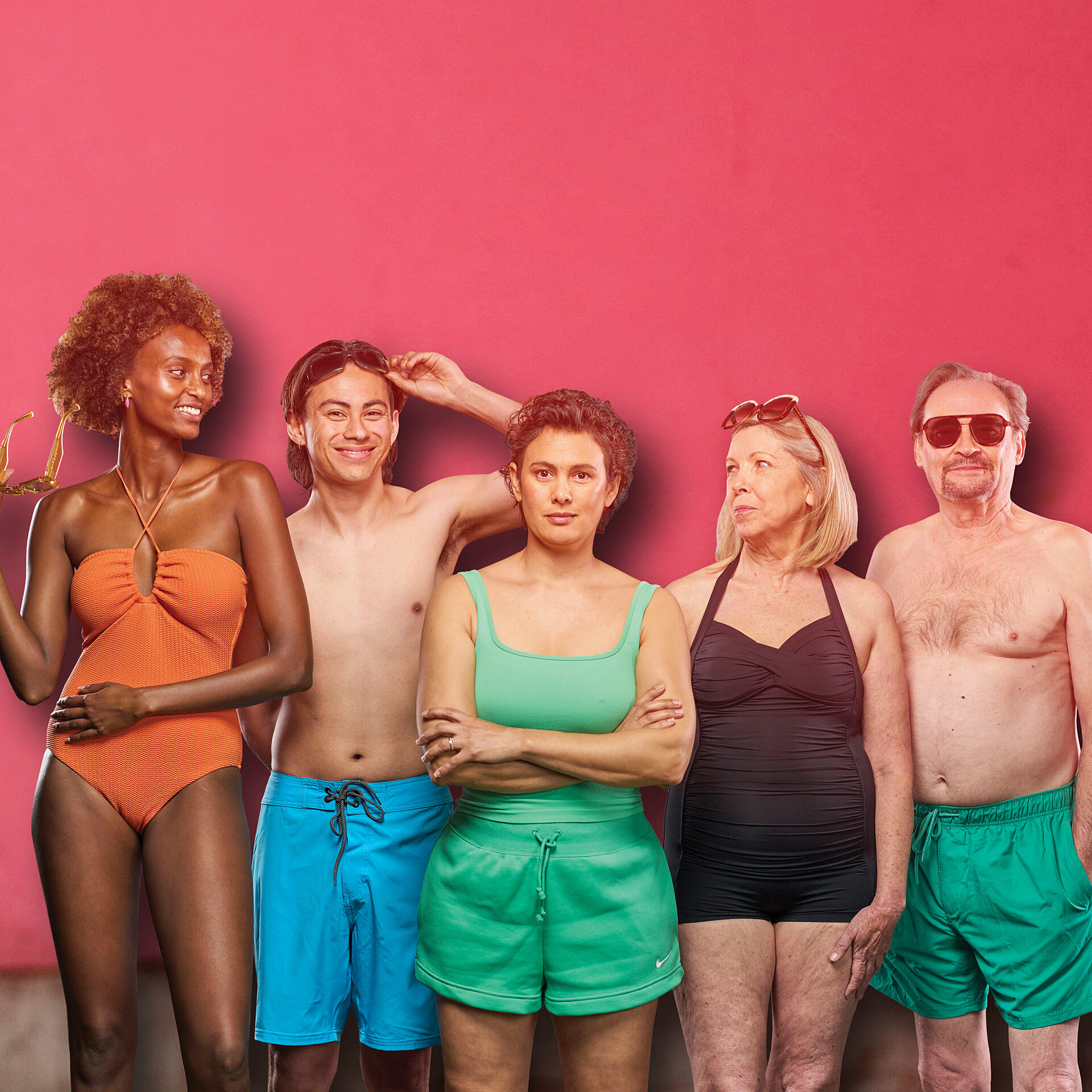 A group of five individuals wearing swimsuits smiling at each other against a pink background.