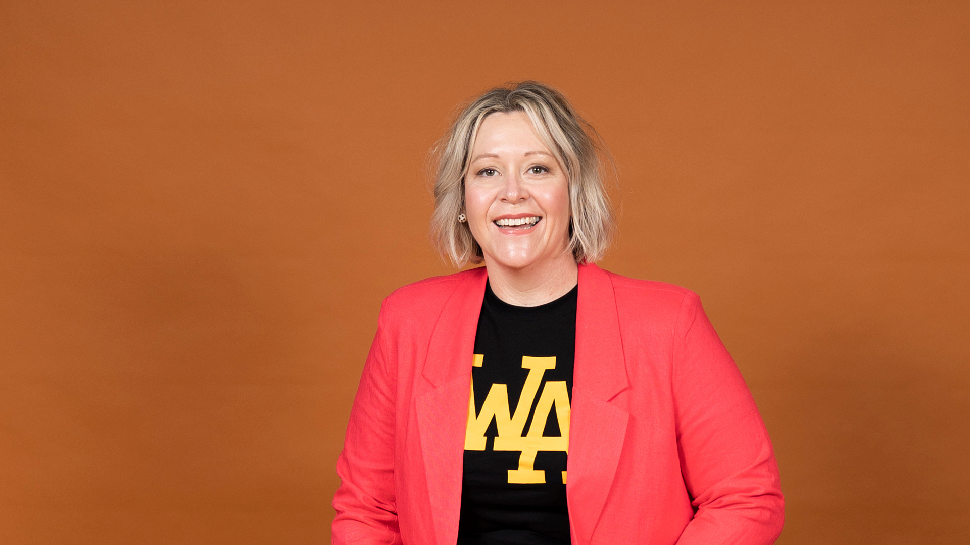 Andrea Gibbs smiling, a white woman with a blonde bob, wearing a black tshirt and red jacket