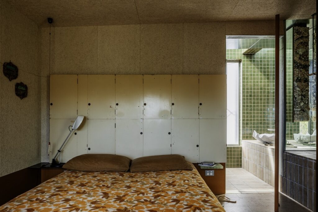 Bedroom with vintage locker-door bedhead and glimpse into green-tiled bathroom, photographed for green magazine issue 105: Timeless by Trevor Mein.