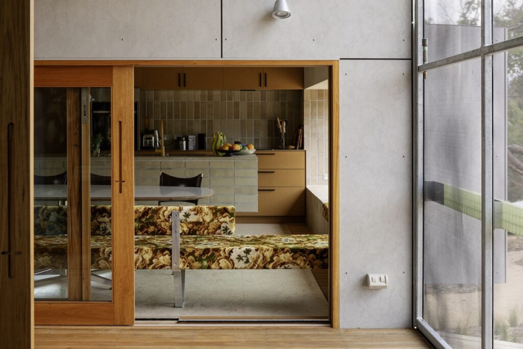 View from deck into dining nook with carpet-covered bench seat and sliding window/door, photographed for green magazine issue 105: Timeless by Trevor Mein.