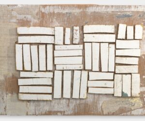 Assemblage of rectangular white-painted wooden fragments arranged in blocks on a weathered timber backing.